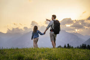 Mann hält die Hand seiner Tochter und geht bei Sonnenuntergang über eine Wiese - DIGF20537