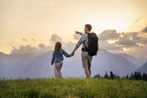 Man holding hand of daughter and walking in meadow at sunset - DIGF20537