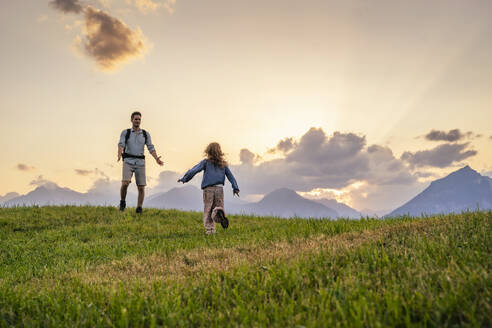 Mädchen läuft auf den Vater zu, der im Gras vor den Bergen steht - DIGF20544