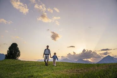 Vater und Tochter spazieren im Gras vor einem Gebirge - DIGF20546