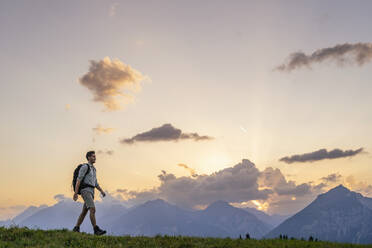 Explorer hiking in meadow by mountain range at sunset - DIGF20549