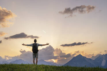 Wanderer mit ausgestreckten Armen und Blick auf eine Bergkette auf einer Wiese - DIGF20550