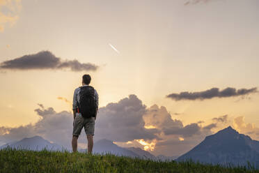 Forscher mit Rucksack schaut auf Bergkette in Wiese - DIGF20551