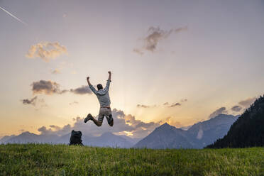 Mann springt auf Gras vor Bergen bei Sonnenuntergang - DIGF20552