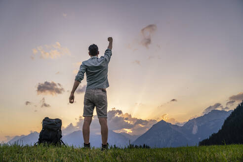 Mann mit erhobener Hand auf einer Wiese bei Sonnenuntergang stehend - DIGF20553