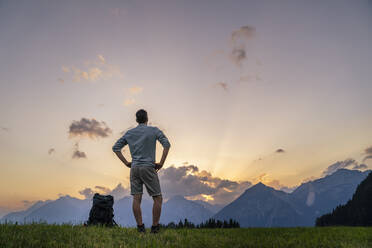 Wanderer mit Händen in den Hüften, der die Berge auf einer Wiese betrachtet - DIGF20554