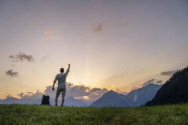 Mann mit erhobener Hand vor einer Bergkette bei Sonnenuntergang - DIGF20555