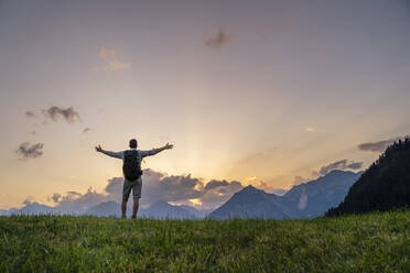 Man with arms outstretched in front of mountains at sunset - DIGF20556