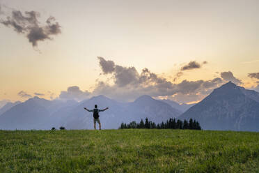 Hiker with arms outstretched standing on grass in front of mountains - DIGF20559