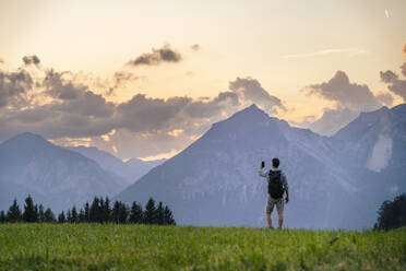 Wanderer, der mit seinem Smartphone auf einer Wiese ein Foto von den Bergen macht - DIGF20562