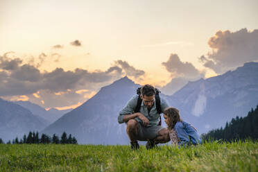 Father and daughter squatting on grass in front of mountains - DIGF20563