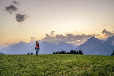 Frau beim Wandern auf einer Wiese bei Sonnenuntergang - DIGF20564