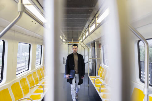 Young man holding folder and walking in train - JPTF01315