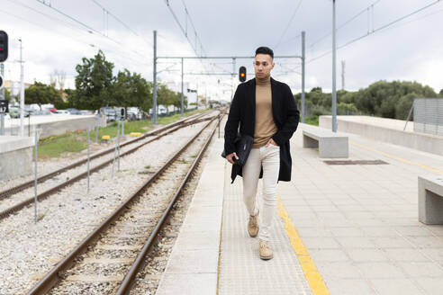 Young man walking on railroad station platform - JPTF01317