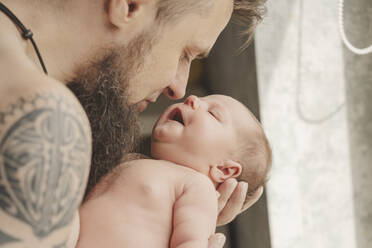 Father with tattoo on arm carrying daughter at home - IHF01656