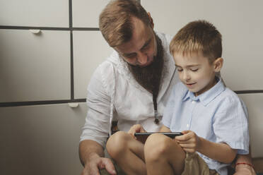Sohn sitzt auf dem Schoß des Vaters und benutzt zu Hause einen Tablet-PC - IHF01664
