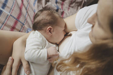 Mother breastfeeding daughter on bed at home - IHF01666