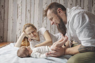 Mutter und Vater spielen mit ihrer neugeborenen Tochter im Bett zu Hause - IHF01670