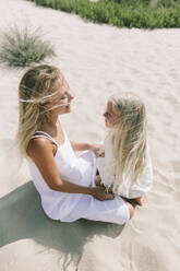 Lächelnde Mutter sitzt mit Tochter am Strand an einem sonnigen Tag - SIF00823