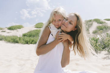 Smiling mother giving piggyback ride to daughter at beach on sunny day - SIF00827