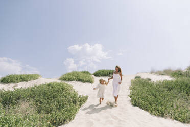 Mutter und Tochter halten sich an den Händen und spazieren im Sand am Strand - SIF00835