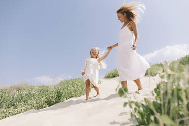 Mutter und Tochter halten sich an den Händen und gehen am Strand spazieren - SIF00842