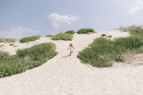 Glückliches Mädchen läuft in der Nähe von Büschen am Strand an einem sonnigen Tag - SIF00849