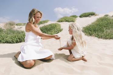 Glückliche Mutter und Tochter spielen mit Sand am Strand an einem sonnigen Tag - SIF00850