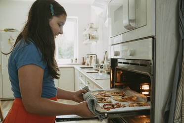 Lächelndes Mädchen beim Pizzabacken im Ofen zu Hause - OSF02122