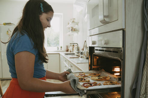 Lächelndes Mädchen beim Pizzabacken im Ofen zu Hause - OSF02122