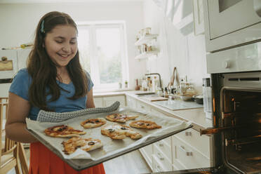 Glückliches Mädchen hält Pizzen auf einem Backblech in der Küche - OSF02123