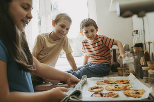 Brüder mit Schwester bereiten in der Küche Pizzen zu - OSF02125