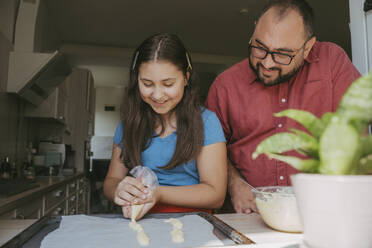 Vater und Tochter bereiten in der Küche Eclairs mit Teig vor - OSF02127