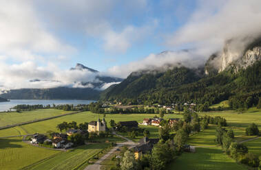 Österreich, Oberösterreich, Sankt Lorenz, Drohnenansicht von Nebel, der sich über einem kleinen Dorf mit Bergen im Hintergrund bildet - WWF06359