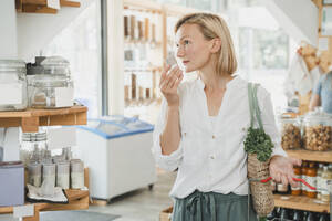 Blonde Frau riecht an einem Warenbehälter und kauft in einem Geschäft ein - NDEF01087