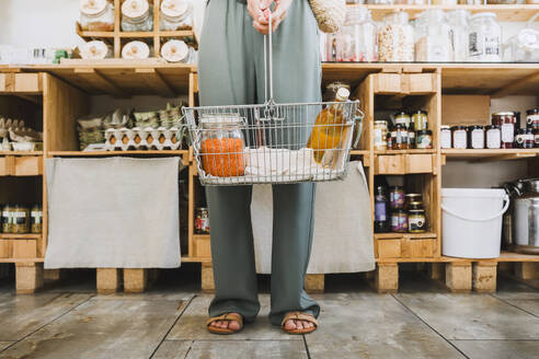 Frau steht mit einem Korb voller Lebensmittel in einem Geschäft - NDEF01098