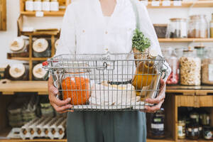 Hands of woman holding basket of groceries in store - NDEF01099