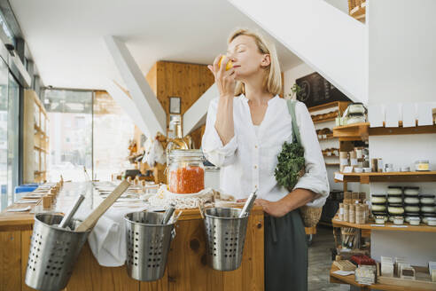 Frau, die an Zitrone riecht, steht an einem Tisch in einem Geschäft - NDEF01108