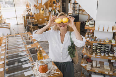 Happy woman holding lemons over eyes at store - NDEF01110