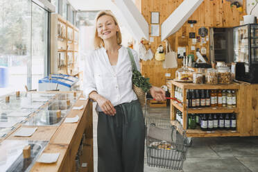 Lächelnde Frau mit Einkaufskorb im Zero-Waste-Laden - NDEF01115