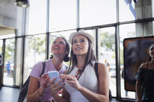 Smiling friends with smart phone standing at railroad station - DCRF01807