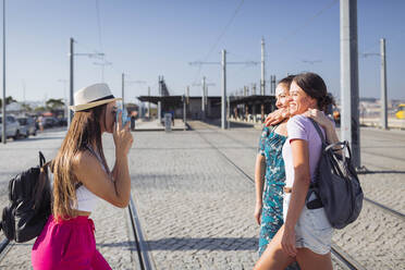 Frau mit Hut fotografiert Freunde mit Kamera an Straßenbahnschienen an einem sonnigen Tag - DCRF01841