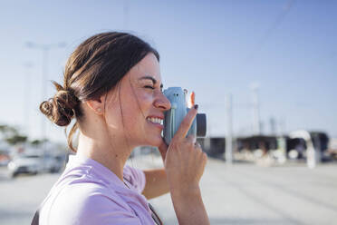 Lächelnde Frau beim Fotografieren mit Kamera an einem sonnigen Tag - DCRF01842