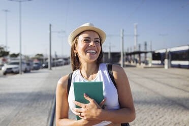 Glückliche Frau mit Hut und Buch an einem sonnigen Tag - DCRF01844