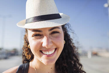 Smiling curly haired woman wearing hat on sunny day - DCRF01850