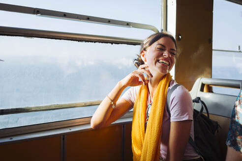 Happy woman sitting in train next to window - DCRF01871