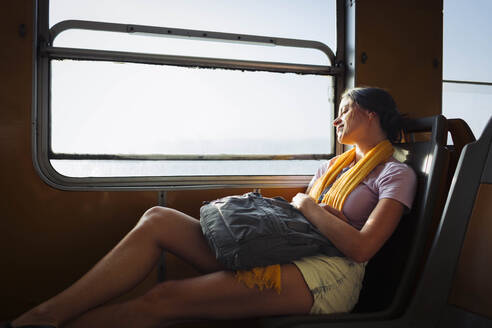 Young woman with backpack relaxing in train - DCRF01880