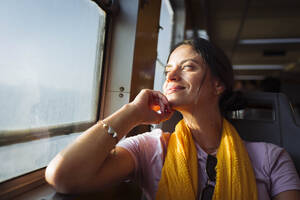Lächelnde Frau mit Hand am Kinn schaut durch das Zugfenster - DCRF01882