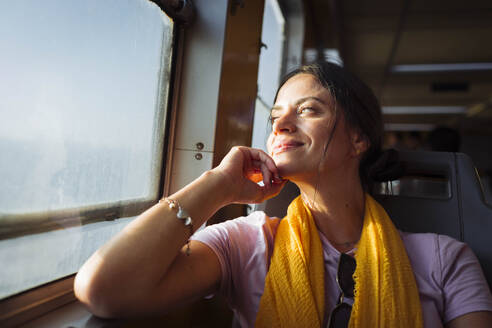 Smiling woman with hand on chin looking through train window - DCRF01882
