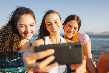 Happy woman taking selfie with friends through smart phone on sunny day - DCRF01894